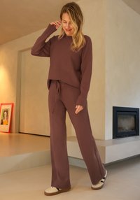 Mauve gebreide trui en bijpassende broek met een taillekoord, voorzien van lange mouwen en wijde, uitlopende pijpen, gecombineerd met casual sneakers.