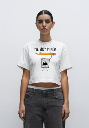 Witte cropped T-shirt met daarin een cartoonpersonage dat een gele pen vasthoudt, met zwarte tekst die "ME HOY MINOY" boven de afbeelding leest.