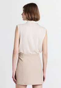 Top senza maniche beige con strisce verticali, abbinato a una gonna attillata di un beige chiaro. Presenta un collo alto e sottili dettagli di texture.