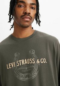 Olivewoblubna koszulka z grafiką przedstawiającą podkowę oraz napisem "Levi Strauss & Co." w beżowym kolorze. Wykonana z bawełny, z krótkim rękawem.
