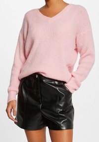 Pull rose tricoté avec encolure en V et épaules tombantes, associé à un short taille haute en simili cuir noir avec coutures avant et poches.