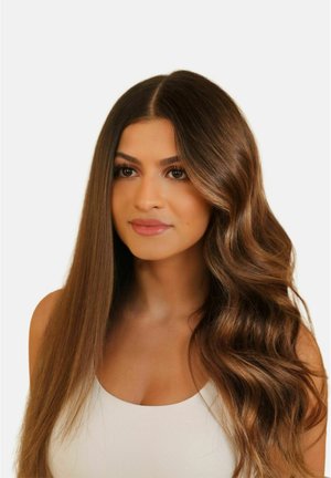 Vrouw met lang bruin haar, aan de ene kant stijl en aan de andere kant los golvend, gekleed in een witte mouwloze top tegen een effen achtergrond.