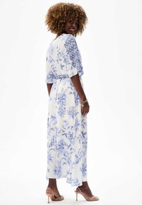 Florale maxi jurk in het wit met blauwe patronen, met een ontspannen fit, losse mouwen en een tailleband. Gecombineerd met naakte hoge hakken.