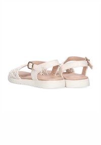 Sandalias blancas con correas trenzadas y hebilla ajustable en el tobillo. Suela plana con un acabado texturizado y forro interior suave. Se muestra vista trasera.