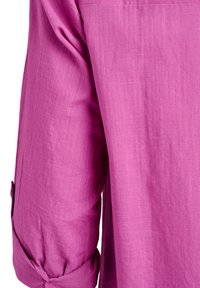 Fuchsiová košeľa s dlhými rukávmi, ktorá má textúrovanú látku, detail srolovaných manžiet a voľný strih. Ľahko pokrčený vzhľad.