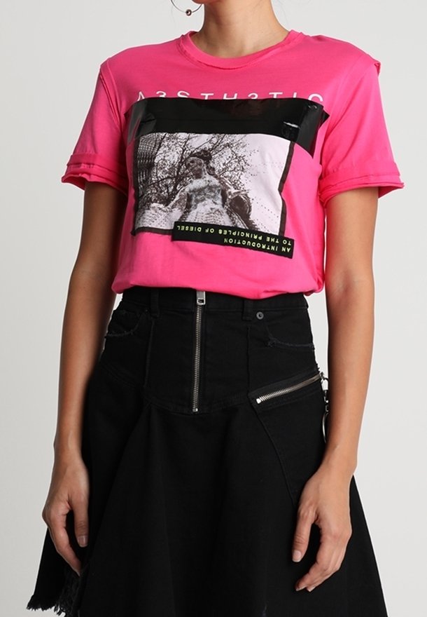 Rosa grafisk t-shirt med en svart rektangel med tryckdesign, korta ärmar och rundad halsringning, ihop med en svart kjol.