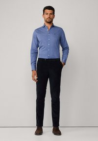 Chemise bleu clair à manches longues avec col, pantalon en velours côtelé noir et chaussures marron. Lignes épurées et design ajusté, sans motifs visibles.