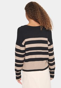 Pull rayé avec de larges lignes horizontales noires et beiges, ourlet côtelé et coupe décontractée. Texture en tricot, encolure bateau et manches longues.