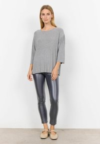 Top gri, texturat, supradimensionat, cu mâneci trei sferturi, asortat cu leggings strânți, lucioși, de culoare gri închis și pantofi bej cu talpă joasă.