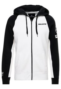 Huvtröja med dragkedja som har en svart-vit färgblockdesign, tillverkad i bomull, med framfickor och logotypdetaljer på ärmarna.