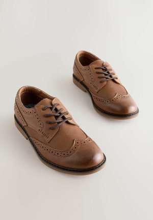 Hnědé kožené boty s hladkým povrchem, zdobené perforovaným vzorem, kulatou špičkou a hnědými tkaničkami, na kontrastní podešvi.