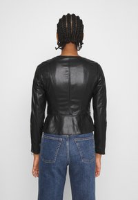 Černá kožená bunda s peplum designem, dlouhými rukávy, švovým detailem a hladkou texturou. Nositá přes modré džíny.