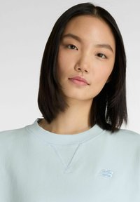 Felpa azzurro chiaro in tessuto morbido con scollo rotondo. Presenta un logo "N" tono su tono sul petto sinistro e polsini e orlo a coste.