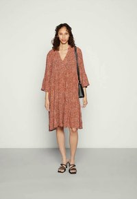 Vestido de cor ferrugem com padrão floral, decote em V e mangas em sino. Acompanhado por uma pequena bolsa transversal preta e sandálias pretas de tiras.