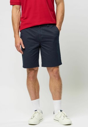 Navy shorts made of cotton blend, featuring a relaxed fit, side pockets, and a clean hem, paired with white sneakers and socks.