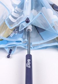 Transparante paraplu met lichtblauwe randen, voorzien van wolkenpatronen. Een stevige metalen steel en een paarse handgreep met "Bluey" erop gedrukt.