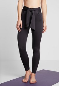 Leggings neri a vita alta con un laccio in vita, texture liscia e design aderente, adatte per l'abbigliamento sportivo o lo yoga.