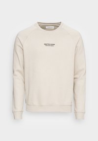 Felpa color crema con maniche raglan, polsini e orlo a costine. Presenta un logo in testo nero sulla parte anteriore. Tessuto morbido e testurizzato.