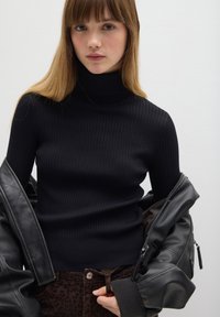 Schwarzer gerippter Wollpullover mit Rollkragen in figurnaher Passform, mit langen Ärmeln, kombiniert mit einer Lederjacke. Strukturierter Stoff mit enganliegendem Sitz.