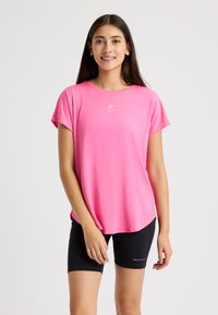 Maglietta sportiva rosa a maniche corte con scollatura rotonda, abbinata a pantaloni corti neri aderenti con dettagli del logo. Tessuto morbido e leggero.