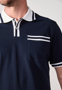 Tumesinine polo särk, millel on kolmest nööbist koosnev kaelus, valge triibuline kaelus ning tasku, millel on kaks valget triipu. Pehme puuvillane kangas.