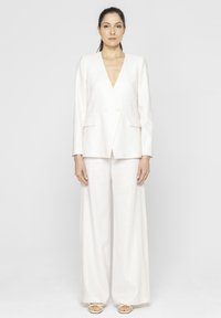 Biały lniany garnitur z głębokim dekoltem w kształcie V, podwójnym zapięciem i szerokimi spodniami, o gładkiej fakturze i czystych liniach.