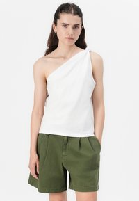 Top alb cu un umăr, realizat din bumbac, cu un detaliu de nod la umăr, asortat cu pantaloni șort plisati de culoare verde măslin. Design simplu și minimalist.