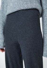Pull gris associé à un pantalon en maille douce gris foncé avec une texture subtile et une ceinture ornée d'un détail minimaliste.