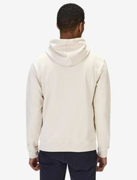 Ljusbeige hoodie med dragkedja, ribbade ärmar och nederkant, tillverkad av mjukt tyg med en slät textur. Bärs tillsammans med mörka byxor.