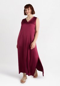 Pitkä burgundinpunainen mekko, jossa on V-pääntie, ilman hihoja, sivurei'itys ja sileä pinta. Yhdistettynä neutraaleihin sandaaleihin.