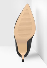 Vue de la semelle d'un talon haut noir à bout pointu avec une semelle beige présentant de fines lignes horizontales antidérapantes.