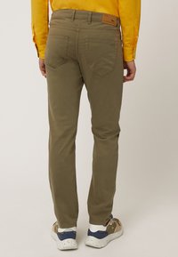 Pantalones ajustados de color verde oliva con una textura suave, que cuentan con bolsillos traseros y un parche de cuero con marca en la cinturilla, combinados con zapatillas en tonos neutros.