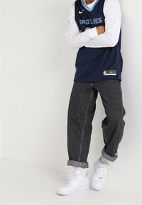 Maillot de basketball navy avec des accents bleus et le texte "GRIZZLIES", associé à un jean gris ample et des baskets blanches, avec des manches retroussées.