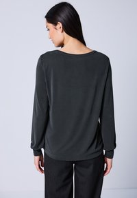Dunkelgrau langärmliges Shirt mit rundem Halsausschnitt, glatter Textur und lässiger Passform, kombiniert mit navyblauen gestreiften Hosen.