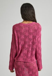 Långärmad, öppet stickad tröja i livfull rosa. Har ett texturerat mönster med öppna vävningar och rund halslinning. Lätt och lös passform.