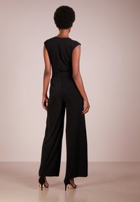 Svart jumpsuit med en åtsittande överdel och vida byxor, tillverkad av ett mjukt material. Har korta ärmar och resårmidja för komfort.