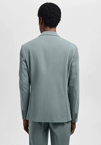 Giacca da uomo in tessuto grigio chiaro. Presenta colli classici a revers, una fessura singola sul retro e maniche lunghe con polsini abbottonati.