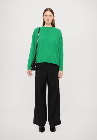 Green oversized sweater, black wide-leg trousers, sleek black handbag, minimalist design. Sweater features dropped shoulders and ribbed cuffs.