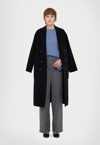 Cappotto nero doppiopetto, maglione blu a maglia, pantaloni grigi a righe sottili e ballerine nere. Design semplice con una vestibilità rilassata.