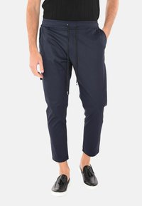 Pantaloni jogger leggeri di colore blu navy con vita elasticizzata, dettaglio con cordino, tasche laterali e gamba affusolata. Indossati con scarpe nere senza lacci.
