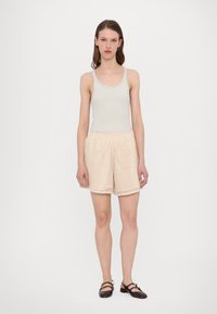 Lichtbeige tanktop en textuur-geweven shorts in een crèmekleur. De shorts hebben een elastische tailleband en een gegolfde zoom. Bruine platte schoenen.