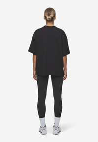 Tricou negru supradimensionat cu mâneci scurte, asortat cu colanți negri strâmți. Ținuta are un design simplu și casual.