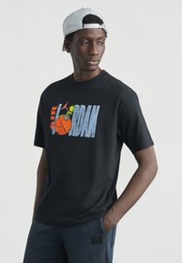 Μαύρο βαμβακερό μπλουζάκι με πολύχρωμο γραφικό "Air Jordan" που απεικονίζει ένα μπάσκετ και παιχνιδιάρικες λεπτομέρειες. Διακρίνεται για την άνετη εφαρμογή και τα κοντά μανίκια.