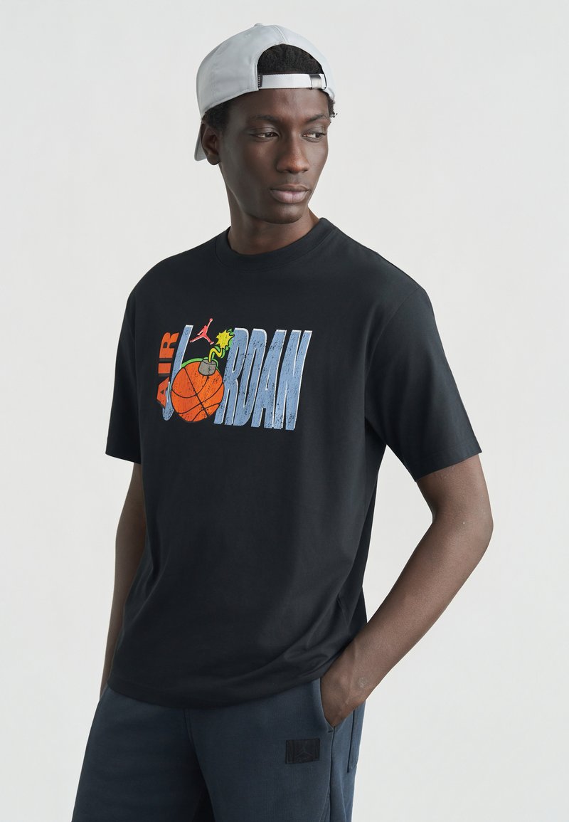 Μαύρο βαμβακερό μπλουζάκι με πολύχρωμο γραφικό "Air Jordan" που απεικονίζει ένα μπάσκετ και παιχνιδιάρικες λεπτομέρειες. Διακρίνεται για την άνετη εφαρμογή και τα κοντά μανίκια.