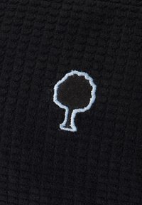 Tessuto nero testurizzato con un piccolo emblema di un albero contornato di bianco ricamato al centro.