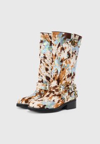 Botas de tobillo de imitación de cuero en tonos marrón y blanco con un patrón, con acentos metálicos, que cuentan con una punta cuadrada y un tacón bajo.