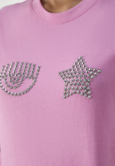 Pink cotton T-shirt featuring silver metal studs in a curved line design and star shape on the front. Smooth texture, crew neck style.