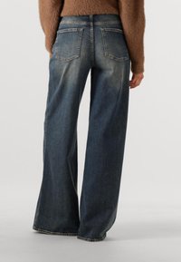Wijdvallende denim jeans in donkerblauw met een vervaagd uiterlijk. Bevat twee achterzakken en rafelige omslagen. Gemaakt van zachte, stevige denim stof.
