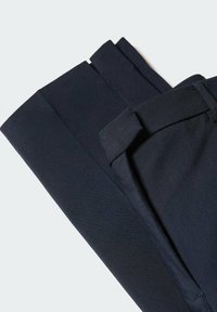 Pantalon de costume bleu marine foncé plié avec une ceinture visible, des passants de ceinture et des poches sur un fond clair uni.