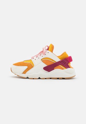 Sneaker basso con pannelli arancioni, gialli e bianchi, lacci rosa e cinturino posteriore rosa scuro su sfondo bianco.